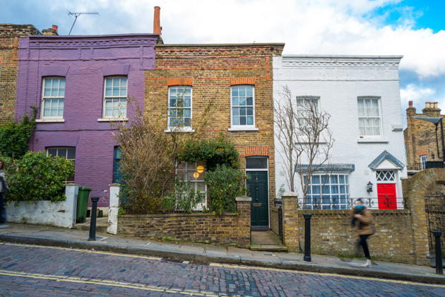 A row of colorful terraced houses, with one painted purple, one left in exposed brick, and another painted white with a bright red door.