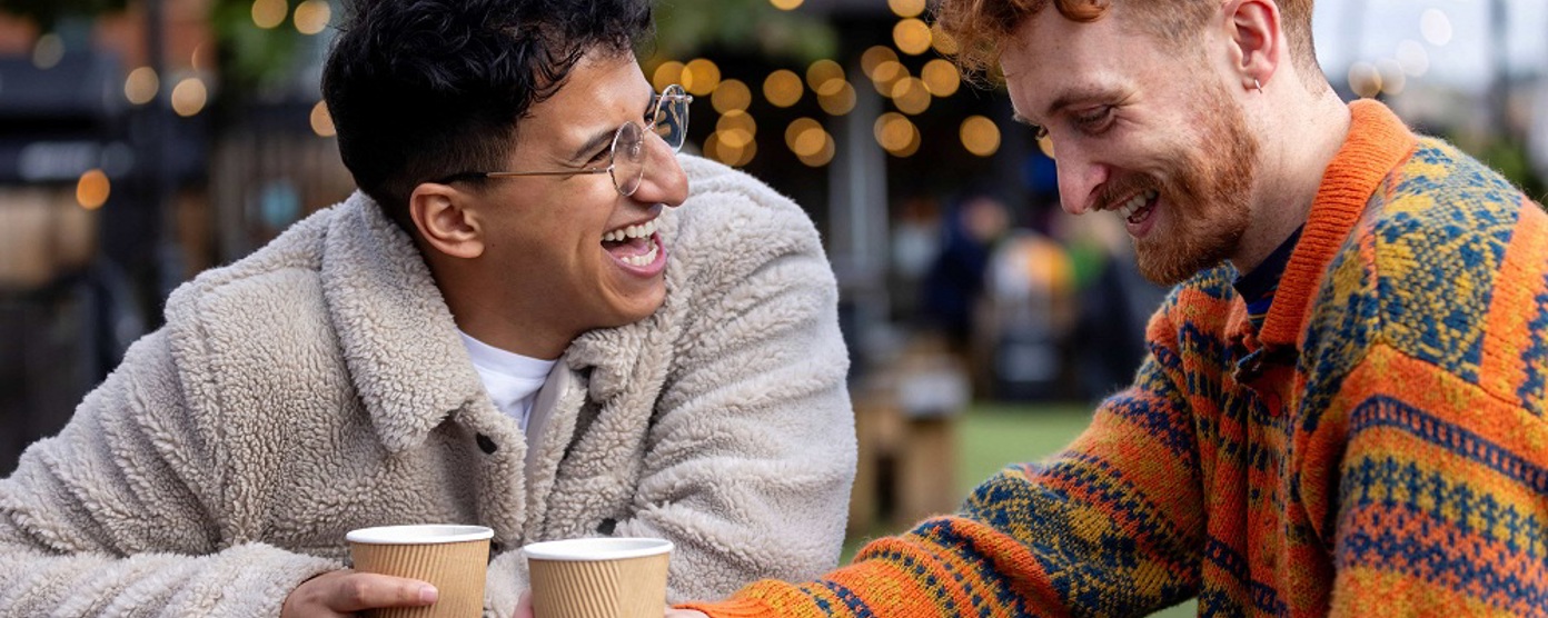 two men smiling over coffee in a park